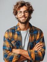 A young man with curly brown hair and a beard smiles at the camera while wearing a plaid shirt photo