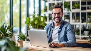 A man smiles while working on a laptop at a desk in a bright and modern office photo