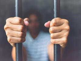 A close-up photo of a persons hands gripping the bars of a prison cell, conveying a sense of confinement and longing for freedom