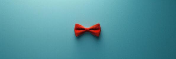 A single red bowtie sits on a teal background, creating a minimalist and stylish image photo