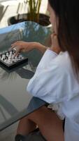 A woman is completely concentrated while enjoying a game of chess outside at a table video