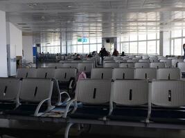 Waiting room at airport with chairs and people in background. Perfect for travel and transit content. Airport seating area filled with passengers. Capture bustling atmosphere of an airport terminal. photo