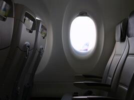 window in plane is from inside, empty chairs are visible for travel and aviation content view of illuminator showing and comfort of cabin, tranquility and spaciousness through scenes with illuminator. photo