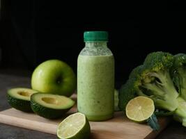 Nutritious green smoothie in bottle, surrounded by avocado, lime, broccoli, apple, cucumber. Ideal for smoothie lovers and wellness content. Emphasize health benefits and freshness of this smoothie. photo