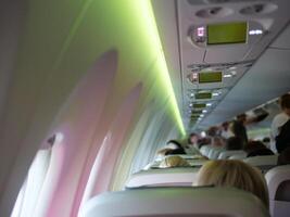 Plane cabin with people sitting, stewardesses in background. Great for aviation and travel content. Plane interior featuring passengers and crew, providing a glimpse into in-flight plane experience. photo