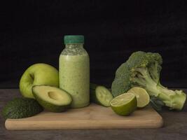 Green smoothie in bottle, surrounded by fresh avocado, lime, broccoli, apple, cucumber Perfect smoothie for health and wellness content Highlighting ingredients for nutritious and refreshing smoothie. photo
