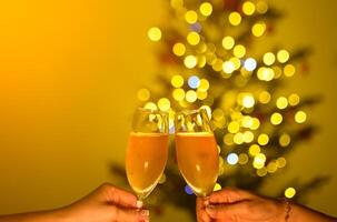 Hands holding glasses of champagne in front of Christmas tree with yellow bokeh lights. Christmas and New Year celebration concept photo