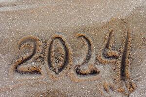 Happy New Year 2024, lettering message handwritten on the beach Numbers 2024 year sand background. photo