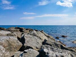 Large stones on the seashore on the background a blue sky with white clouds. Large stones on the seashore on the background a blue sky with white clouds.The Ligurian Sea, Italy. photo