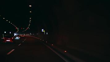 Cars driving through a well-lit tunnel with illuminated signs and overhead lights, traffic moving smoothly towards the tunnel exit, creating a dynamic urban travel scene. video