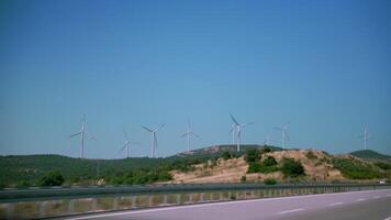 rodovia passagem de vento Fazenda com múltiplo vento turbinas em uma gramíneo encosta debaixo uma Claro azul céu, simbolizando renovável energia e sustentável viagem video