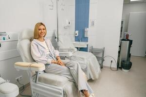 Smiling woman sitting in armchair while waiting for IV infusion during treatment in hospital photo