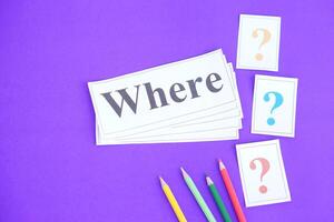 Word card paper with text Where and pencils on purple background. Concept. Teaching aid. Education materials for teach WH question. Asking questions.Suspicious symbol to find answer photo