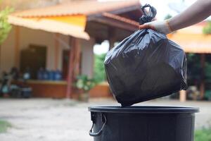 Hand holding garbage black bag putting in to the bin. Concept, garbage management, Keep clean for sanitary and community service for the best environment. Zero waste. photo