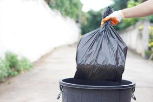 Hand holding garbage black bag putting in to the bin. Concept, garbage management, Keep clean for sanitary and community service for the best environment. Zero waste. photo