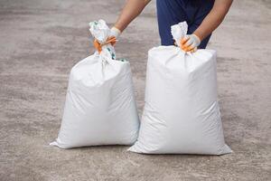 Close up man holds two white White polypropylene sack that contain full of agricultural grains, tied on the top with bamboo rope. Concept, reusable bag for contain crops, fertilizer or others. photo