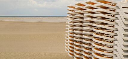Sun loungers stacked on top of each other stand in a row on the seashore on the sand. Sun beds for rent. Abstract background from summer travel. photo
