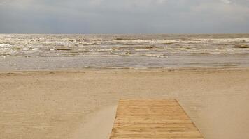 Perspective view of a wooden pier on the coast with sand and sea with waves. Horizon, sea and sky on a cloudy day. Abstract background from summer travel. photo