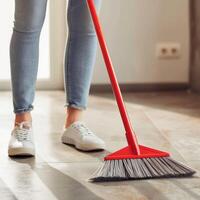 Woman Sweeping Floor with Red Broom in Sunlit Room, Casual Home Cleaning Scene, Relaxed Atmosphere, Cleanliness Concept, Domestic Chore photo
