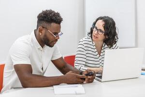 Man and Woman Collaborating on Project in Office Using Laptop and Smartphone photo