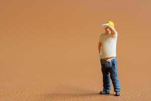 Miniature construction worker. He stands with one hand on his hip while wiping sweat from his forehead photo