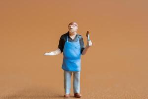 Miniature people , A chef is wearing a blue apron over a black shirt and light-colored pants. The background is a solid, photo