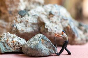 Miniature worker pushing a large rock. Themes of perseverance, strength and labor. This makes it suitable for use in content that involves hard work, challenges, and overcoming obstacles. photo