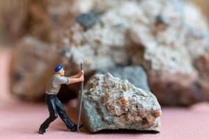 Miniature worker pushing a large rock. Themes of perseverance, strength and labor. This makes it suitable for use in content that involves hard work, challenges, and overcoming obstacles. photo