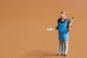 Miniature people , A chef is wearing a blue apron over a black shirt and light-colored pants. The background is a solid, photo