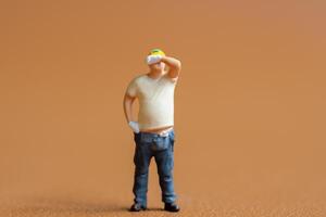 Miniature construction worker. He stands with one hand on his hip while wiping sweat from his forehead photo
