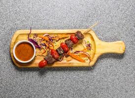 beef fillet satay skewers with chilli sauce served on wooden bard isolated on grey background top view of hong kong fastfood photo