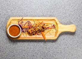 Chicken bbq satay with chilli sauce served on wooden bard isolated on grey background top view of hong kong fastfood photo