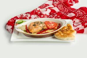 Baked salmon fillet with pita bread, cucumber, tomato in a dish isolated on colorful table cloth top view on grey background photo