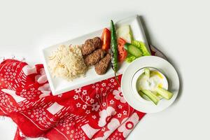 traditional turkish cuisine Izgara Kofte wuth rice, raita and salad in a dish isolated on colorful table cloth top view on grey background photo