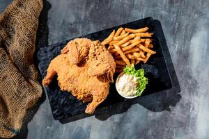 Crispy fried Spring Chicken full with french fries and mayo dip in a black dish top view on dark background fast food photo