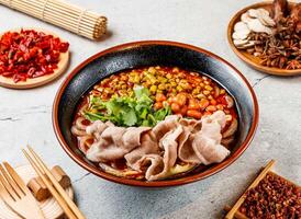 Pork Hot and Sour Noodles with coriander, beans, red chilli, chopsticks and fork served in pot isolated on background side view of taiwanese food photo