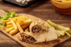 Beef Shawarma with french fries served in a cutting board isolated on wooden table background side view of fastfood photo
