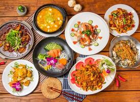Chongqing Boiled Fish, Crab Roe and Tofu Pot, Pineapple Shrimp Balls, Comprehensive sashim, seafood salad, Kung Pao Chicken, Soft Shell Crab, Bean crispy fresh oysters with chopsticks side view photo