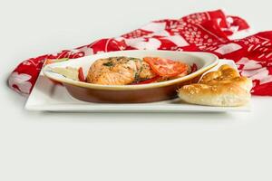 Baked salmon fillet with pita bread, cucumber, tomato in a dish isolated on colorful table cloth top view on grey background photo
