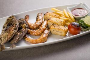 Seafood mix grill with fish tikka, shrimp, prawns, fries, and tomato sauce served in dish isolated on grey background top view of arabic food photo