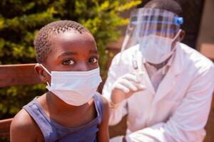 Portrait of a child in a clinic in Africa about to be vaccinated with the doctor beside him. photo