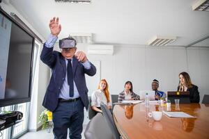 During a conference a businessman uses virtual reality headsets while others observe him photo