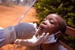 A doctor performs a coronavirus test on a child in Africa and inserts the swab down his throat photo