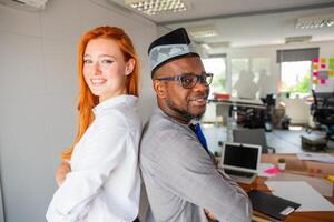 Two colleagues posing smiling in the office back to back, corporate life photo