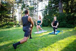 A fitness coach holds a class with two girls and they perform exercises in a public park photo