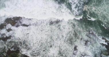 aerial drone view of foam waves on a rocky shore in a cloudy day video