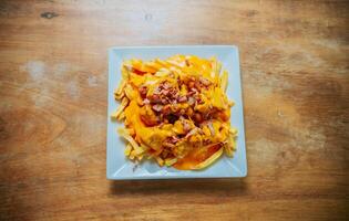 Top view of french fries covered with cheddar cheese and bacon on wooden table. French fries dipped in yellow cheese with bacon on wooden table photo