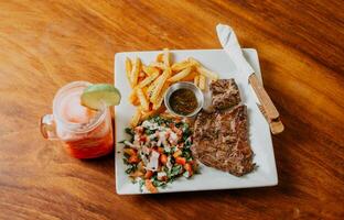 Plate of skirt steak with french fries and drink served on wooden table. Delicious homemade steak with healthy juice photo