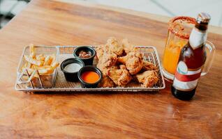 Top view of spicy wings with fries and michelada accompanied with beer served on wooden table photo