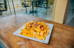 French fries dipped in yellow cheese with bacon on wooden table. Close up of french fries covered with cheddar cheese and bacon on wooden table photo